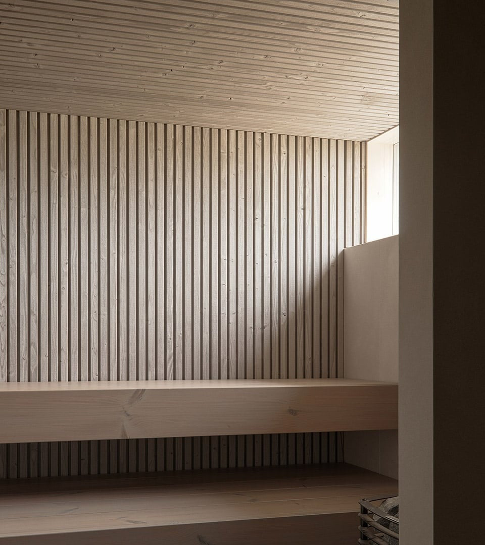 Minimalist wooden sauna interior with UV-treated Nordic spruce slatted walls, built-in benches, and soft natural light.