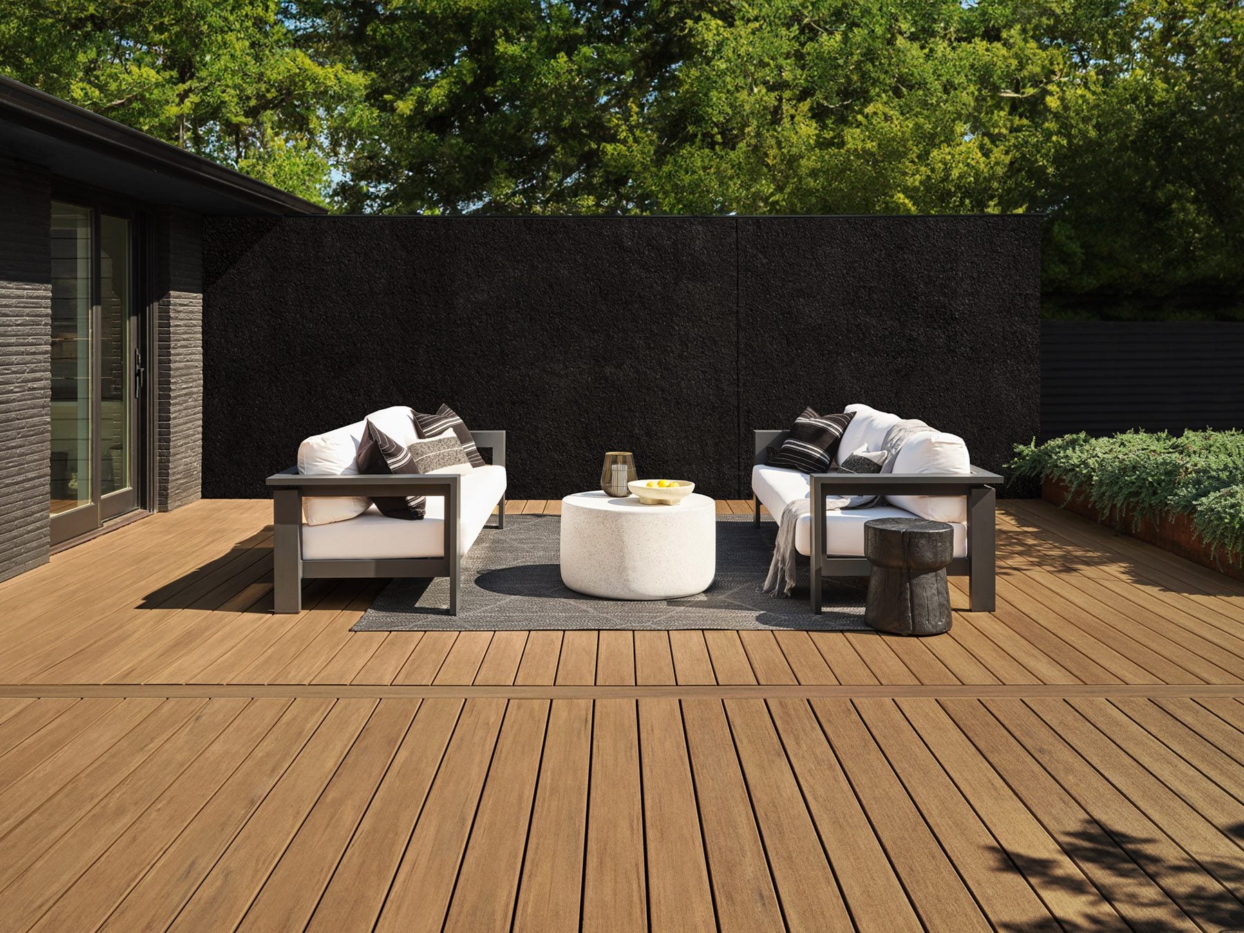 Outdoor patio with brown wood alternative decking, metal-framed seating, cushions, a throw blanket, and potted yellow flowers.