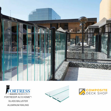 Glass baluster railing and aluminum railing enclose a pool area, with modern buildings behind. Fortress Railing Products logo visible.