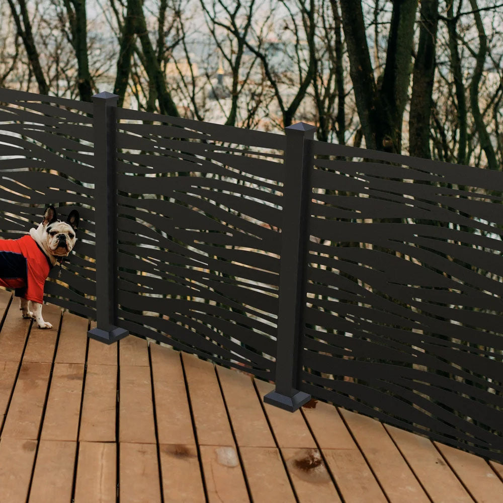 A small dog in a red and black jacket stands by a powder-coated aluminum privacy screen with wavy cutouts on the deck.