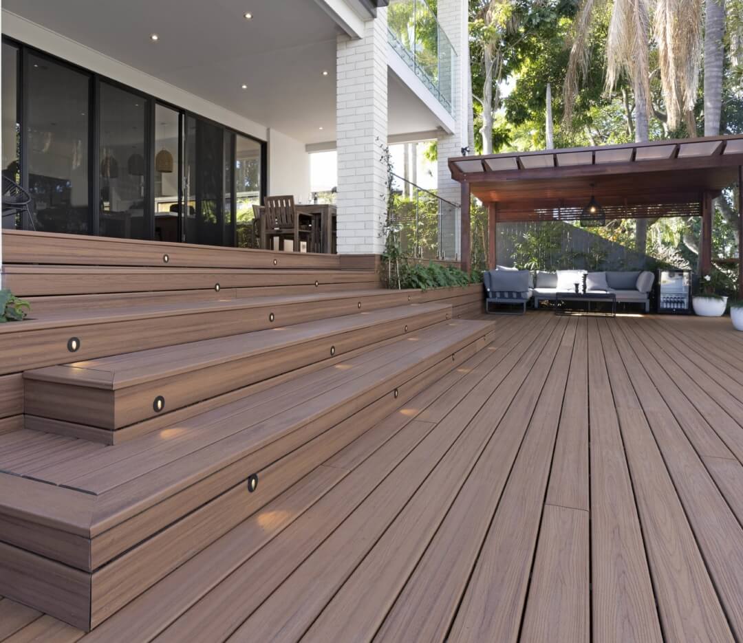 Trex composite decking with wide steps, built-in lights, patio furniture, and a covered outdoor seating area surrounded by greenery.